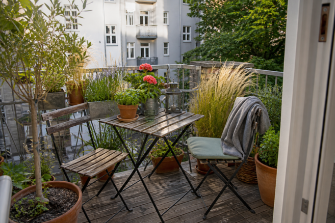 Ein kleiner Stadtbalkon wird mit Pflanzen, Holzmöbeln und wenigen Accessoires gemütlich gestaltet
