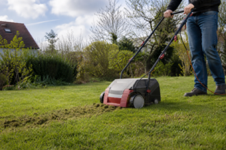 Ein Gartenbesitzer vertikutiert einen trockenen Rasen bei mildem Frühlingswetter [Bildinhalt mit KI erstellt]